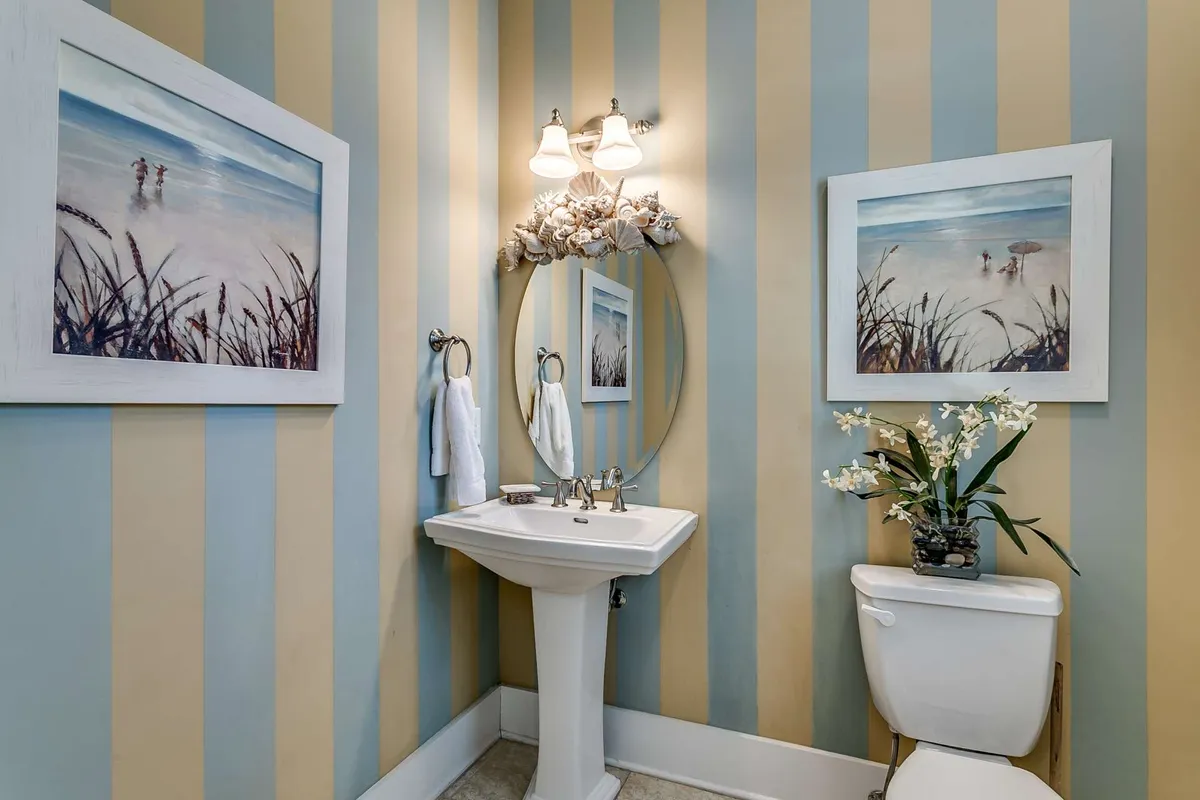 A light-hearted, stylish powder room featuring striped walls, framed paintings, a sink and mirror, and decorative plants—offering a refreshing spot for guests to freshen up.