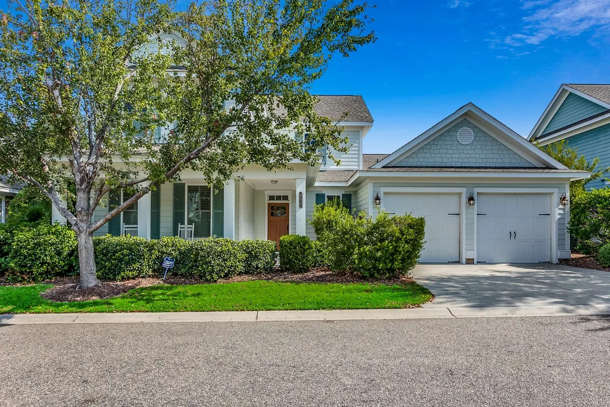 A welcoming front porch looking out onto a landscaped garden, with a double garage in the background. The space is set up for relaxing, socializing, and enjoying sunset views, highlighting the home's inviting exterior amenities.