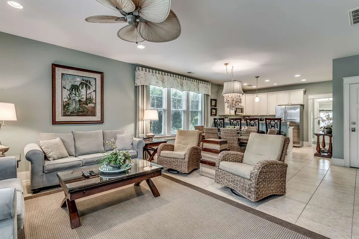 The image showcases a beautifully decorated living room with a plush sofa, elegant coffee table, striking artwork, and a statement chandelier. The space is designed for guests to relax, socialize, and celebrate together, conveying a warm, welcoming atmosphere ideal for gatherings and special occasions.