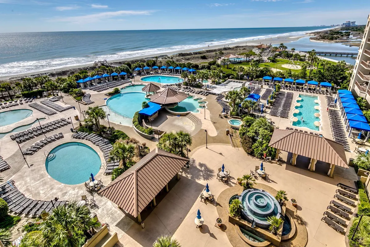 This exterior image features the resort’s iconic pool complex, with multiple swimming pools, palm trees, sun loungers, and views extending to the beach and ocean. The area looks lively and inviting, perfect for relaxation, swimming, and socializing.