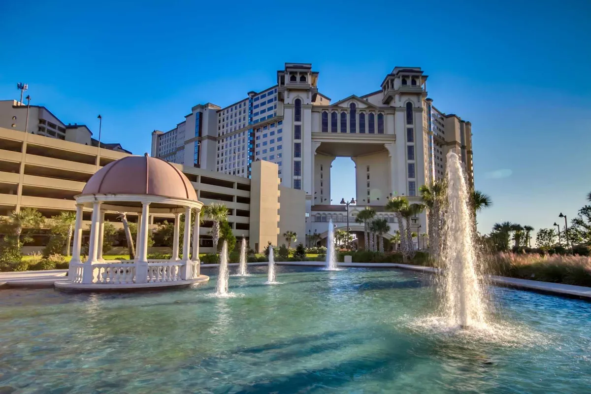 A peaceful resort exterior scene showcasing a fountain, a charming gazebo, and the facade of a well-maintained building. The area is designed for relaxation, offering quiet spots to unwind and enjoy the outdoors.