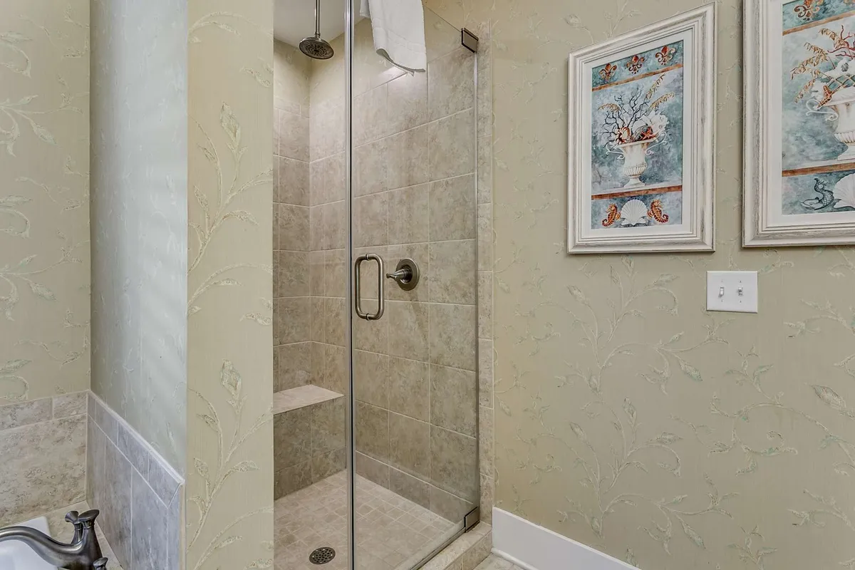 A tranquil, spa-like bathroom interior featuring a glass shower enclosure, decorative wall art, and textured wallpaper. The space exudes a calming, luxurious feel ideal for relaxation and rejuvenation.