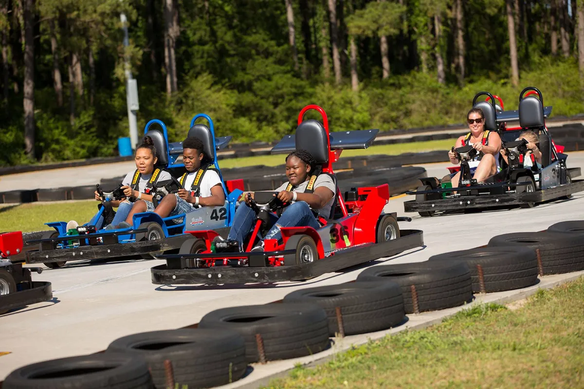 A lively go-kart racing track with families and participants zipping around, set in an open, outdoor environment. The energy and excitement of the scene highlight competitive fun and memorable shared experiences.