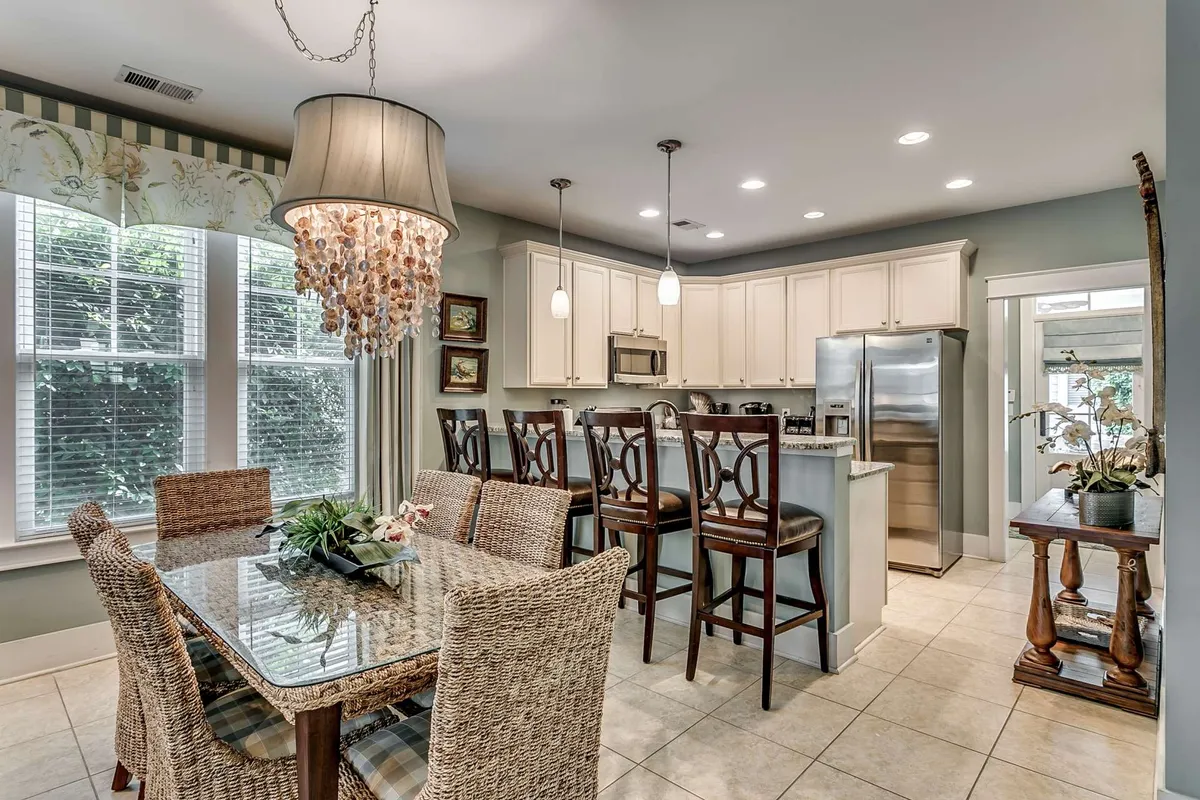 A contemporary dining area seamlessly connected to the kitchen, with a large dining table, stylish chandelier, and expansive windows. The kitchen island offers extra seating, and the overall space is bathed in natural light, emphasizing the open floor plan. The layout supports both intimate family meals and festive gatherings.